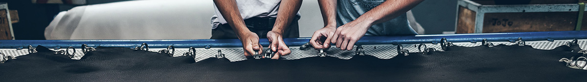 Two men stretching black cow hide.